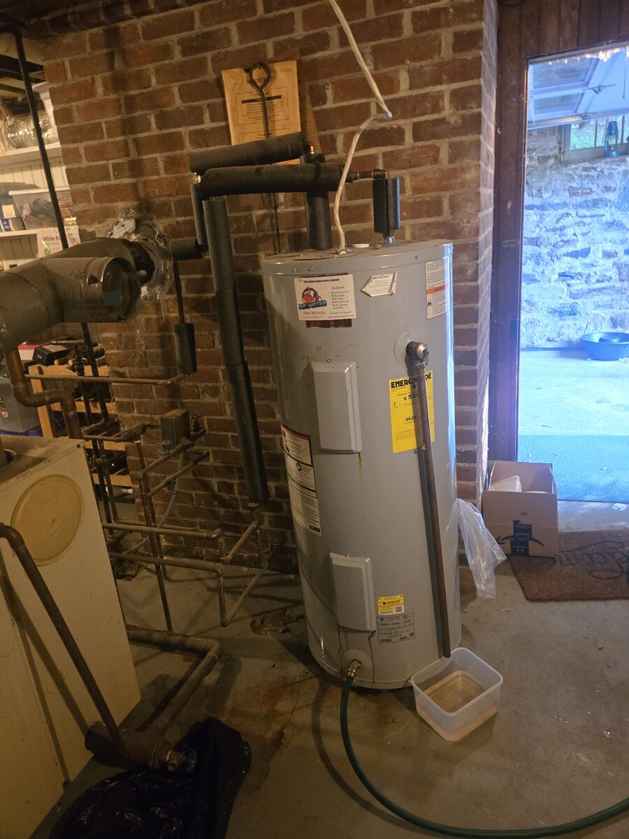 Electric tank water heater in a brick basement with a garden hose on the drain valve