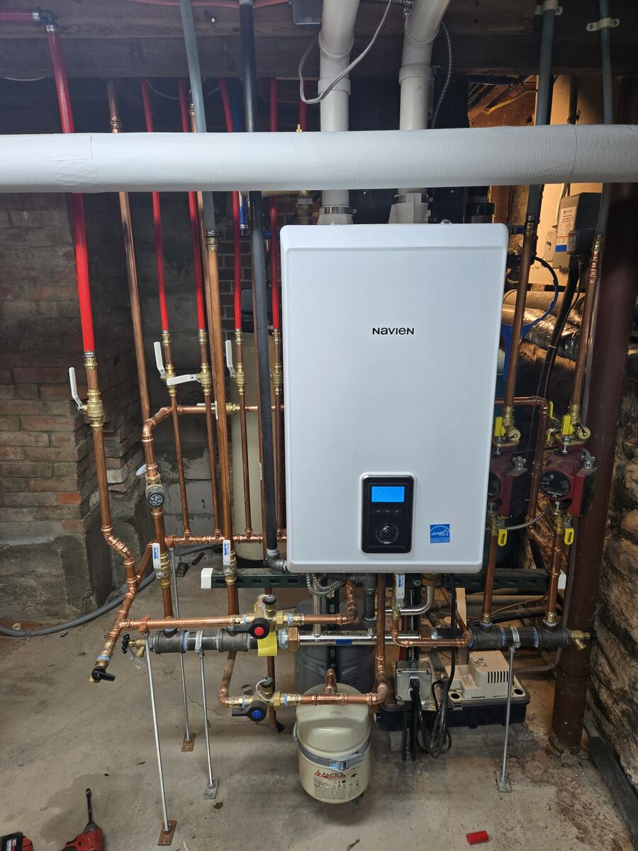 Wall-hung combi unit installed among copper and red and blue PEX lines in an older basement