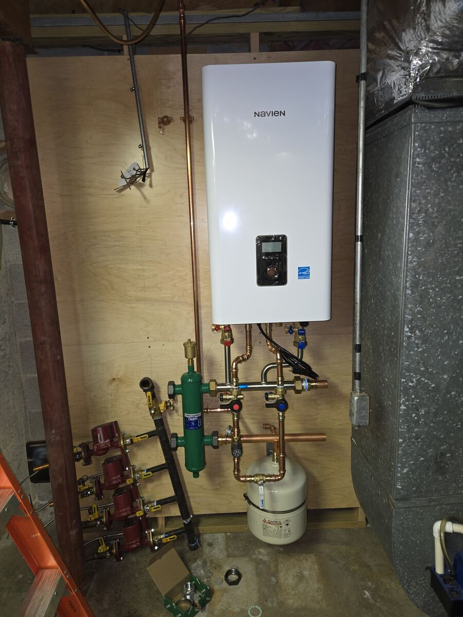 New wall-hung combi unit on a plywood board with copper piping and pumps being connected